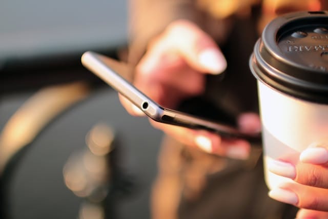 close up image of a person's hand holding a cell phone and a cup of coffee