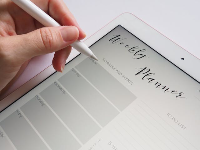 closeup image of a tablet with a weekly planner on it, part of a hand holding a stylus