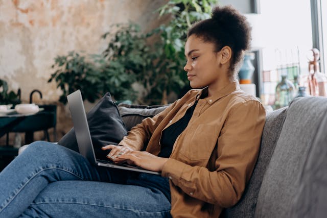 woman sitting on a grey couch in a cozy setting using a laptop